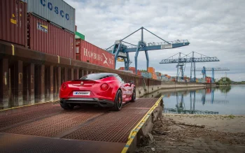 Красная Alfa Romeo 4C на фоне грузового порта в пасмурный день