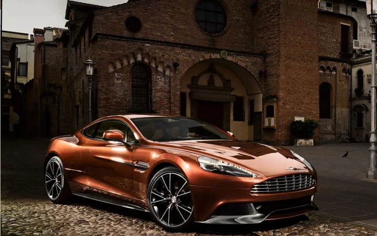 a copper-colored aston martin vanquish in an old italian square, aston martin vanquish, areas, aston martin, cars, automobiles, discs, wheels, evening, evenings, twilight, dus, headlights, houses, buildings, sports cars, streets, auto, vehicles