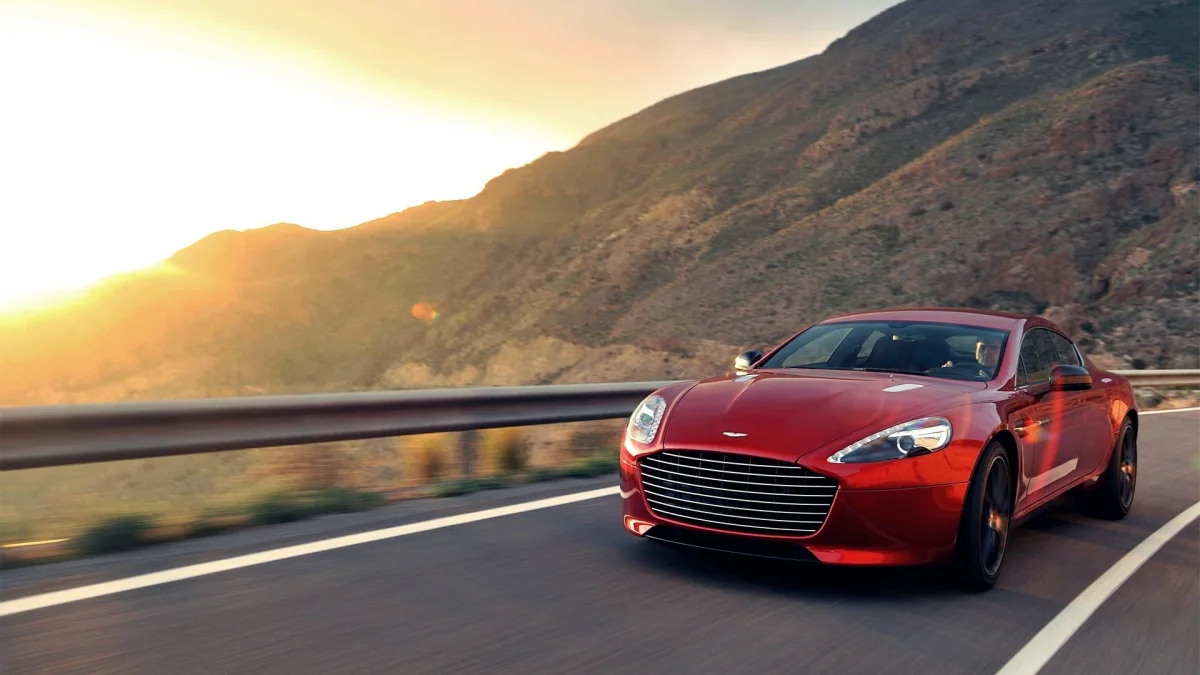 A red Aston Martin Rapide on a mountain road, bathed in the glow of the setting sun