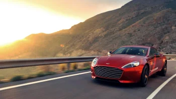 A red Aston Martin Rapide on a mountain road, bathed in the glow of the setting sun