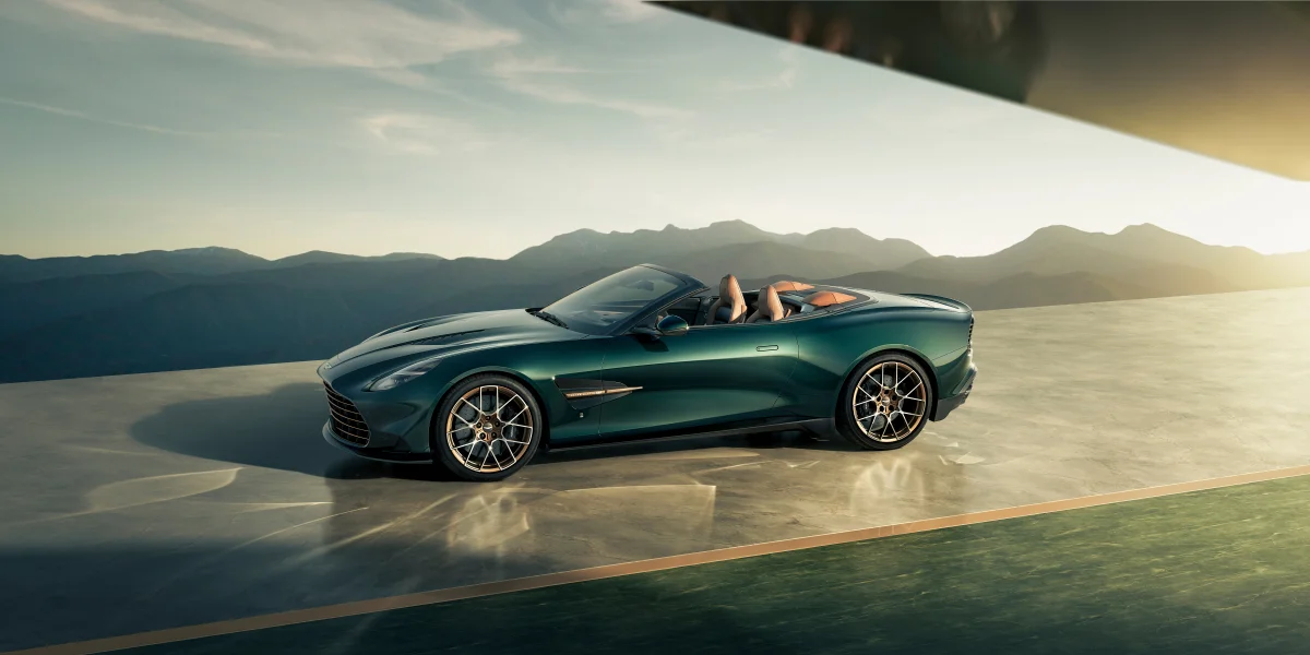 A green Aston Martin DB12 Volante convertible against a backdrop of mountain peaks