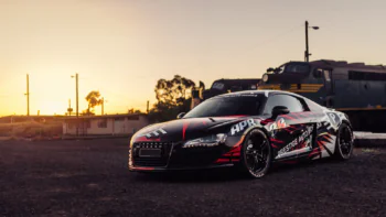 Спортивное купе Audi R8 на фоне заката и старого локомотива