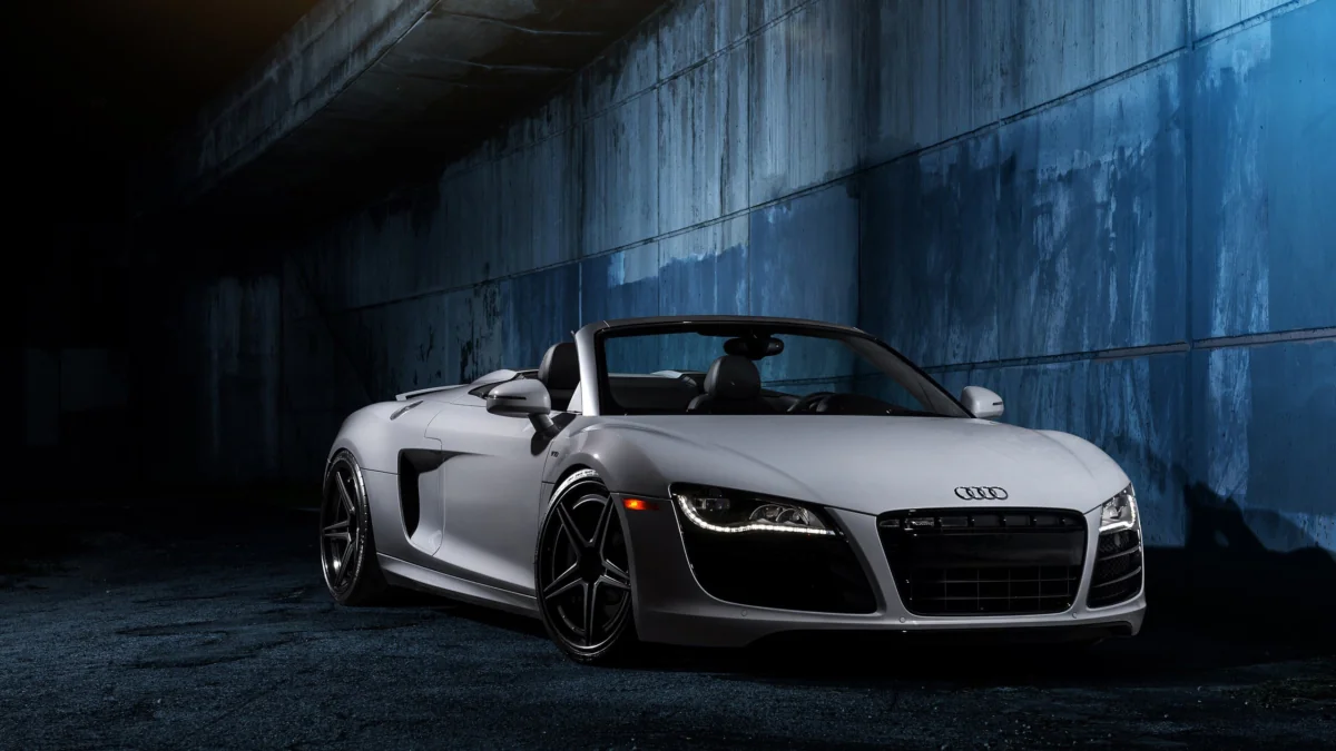 Серебристый кабриолет Audi R8 в свете ночных огней у бетонной стены