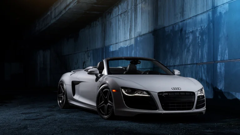 Серебристый кабриолет Audi R8 в свете ночных огней у бетонной стены