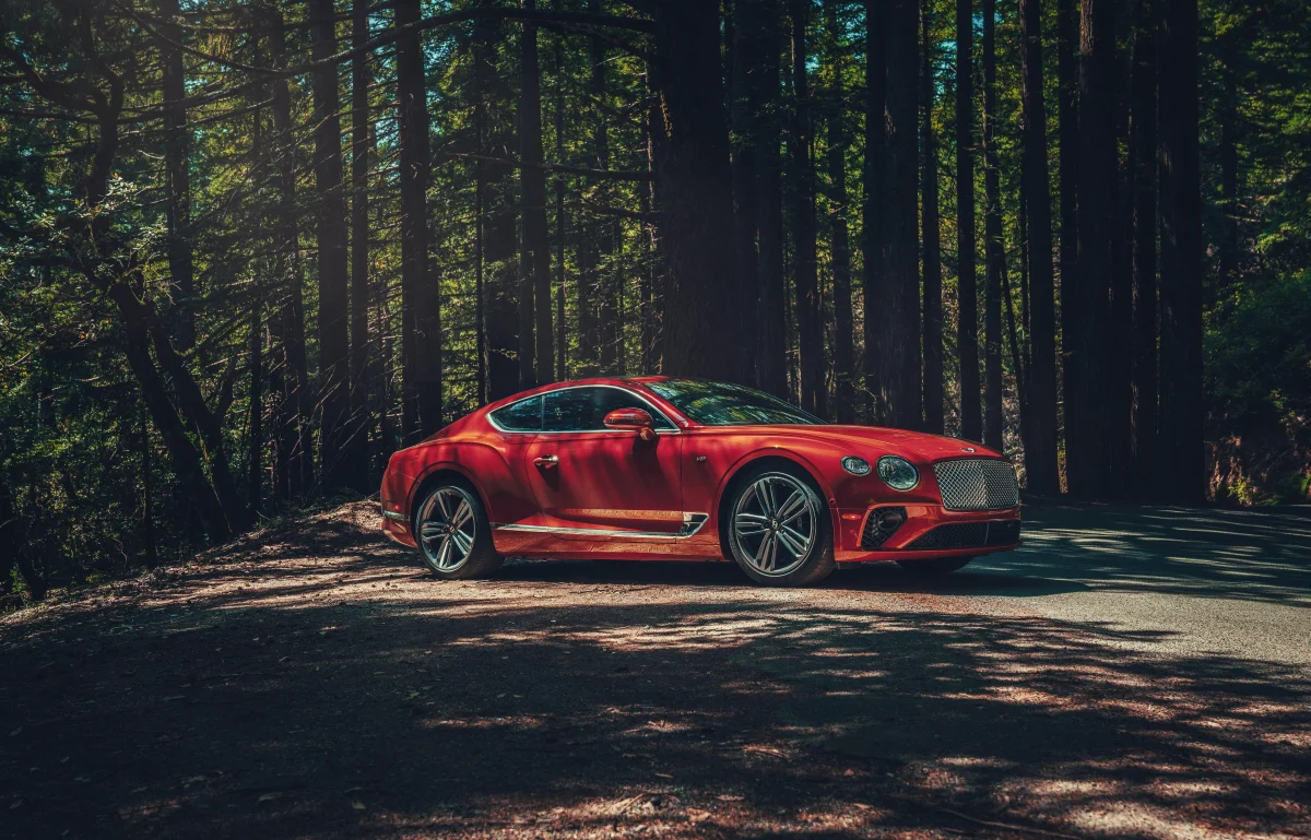 A red Bentley Continental GT on a forest road