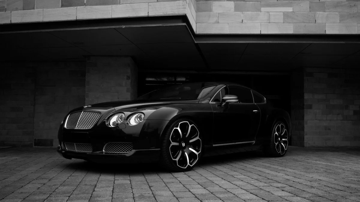 A black Bentley Continental GT in the shadow of a modern stone building