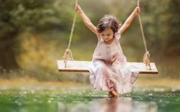 A little girl on a swing over the smooth surface of the water in the park