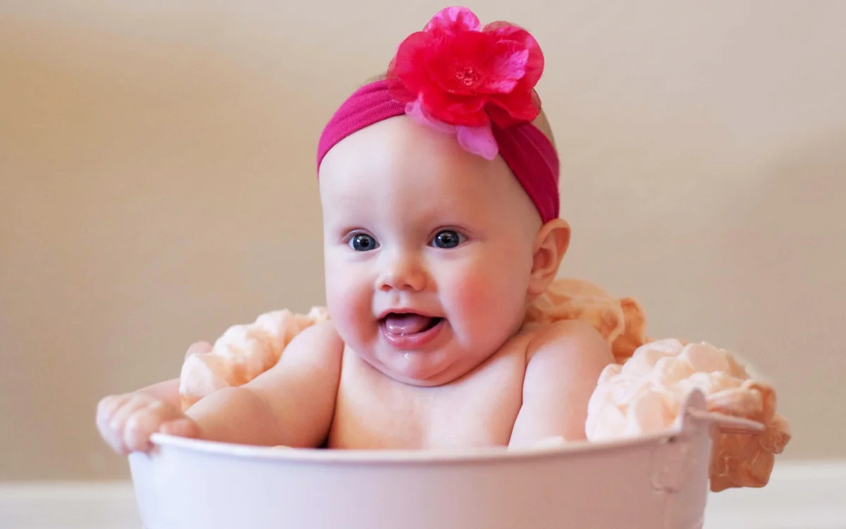 A toddler wearing a pink headband with a flower in a home setting