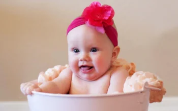 A toddler wearing a pink headband with a flower in a home setting