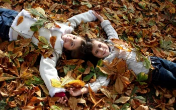 Two sisters are lying on a carpet of fallen autumn leaves