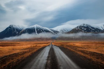 A dirt road leading to the snow-capped Icelandic mountains