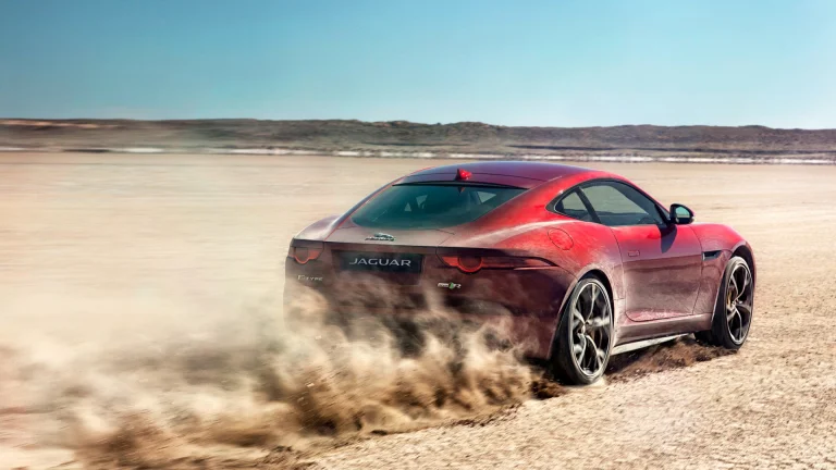 A red Jaguar F-Type kicks up a cloud of dust on the salt flats