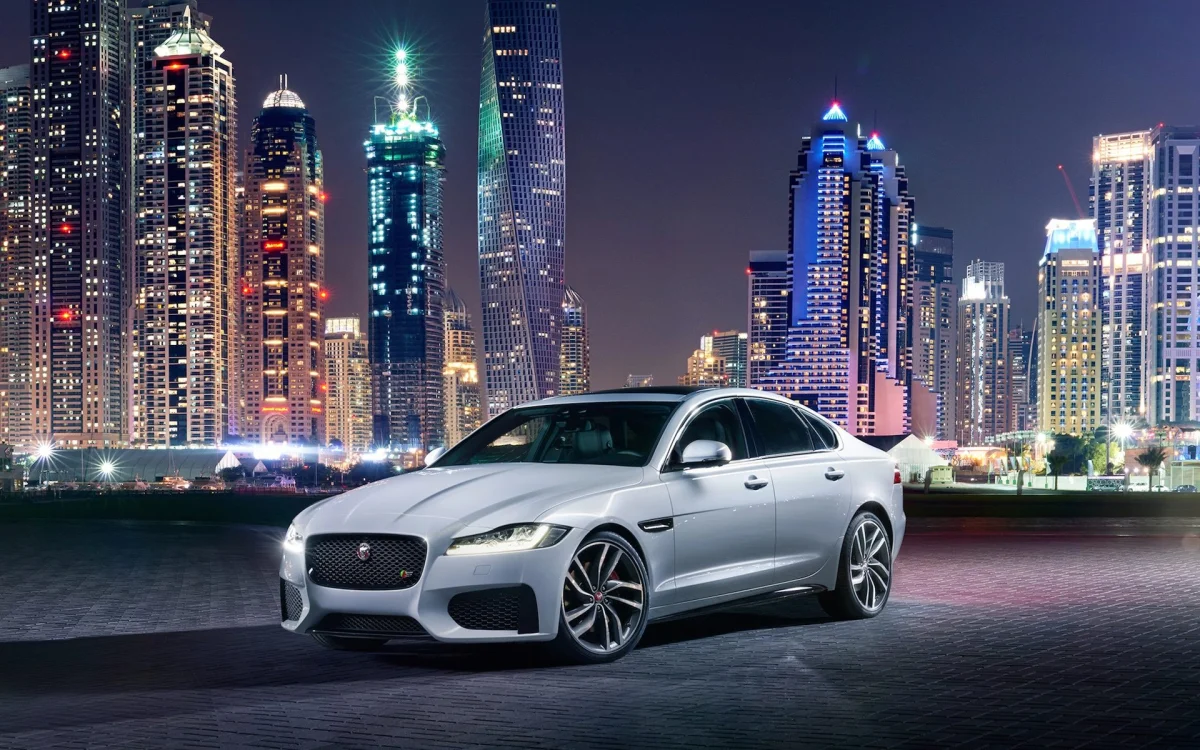 Серебристый Jaguar XF на фоне ночных небоскребов Дубая