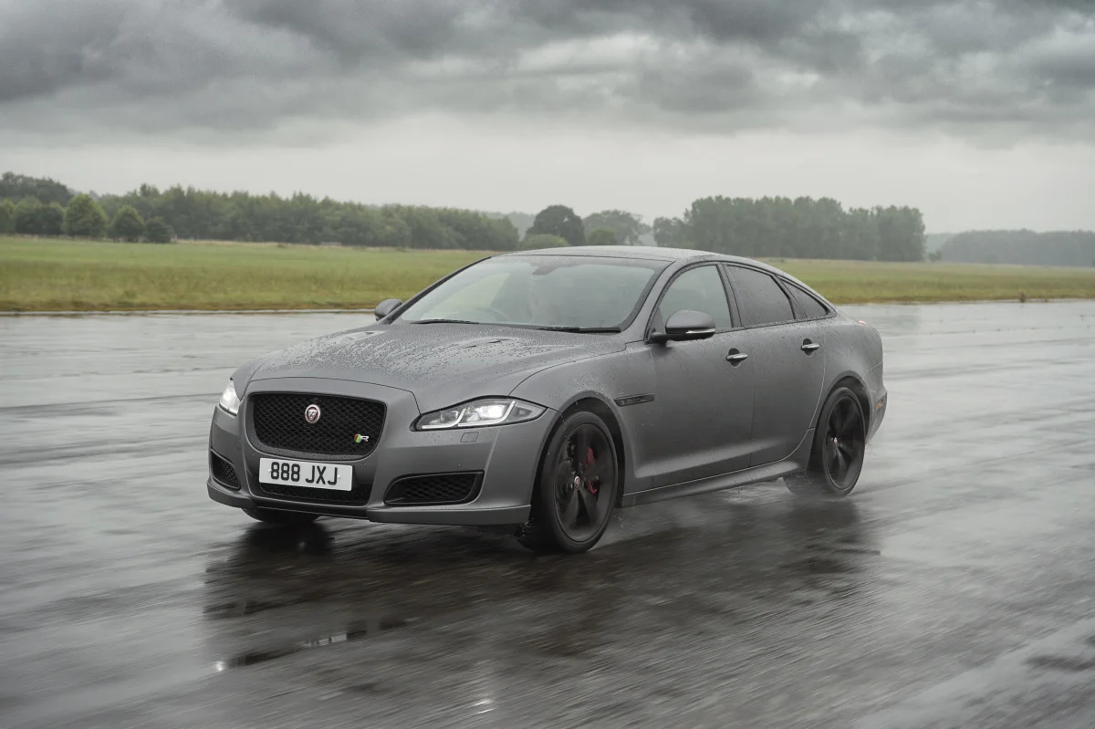 Серый Jaguar XJ на мокром асфальте под пасмурным небом