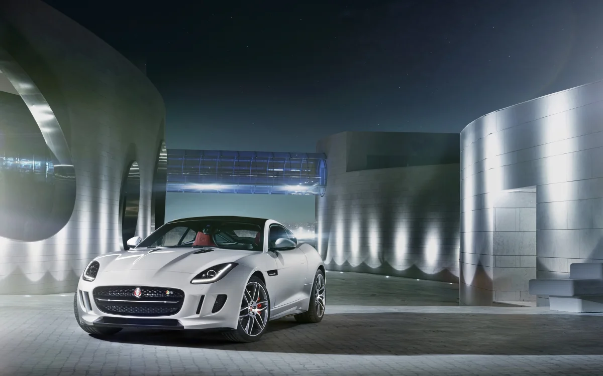 Білий Jaguar F-Type на тлі футуристичних будівель уночі