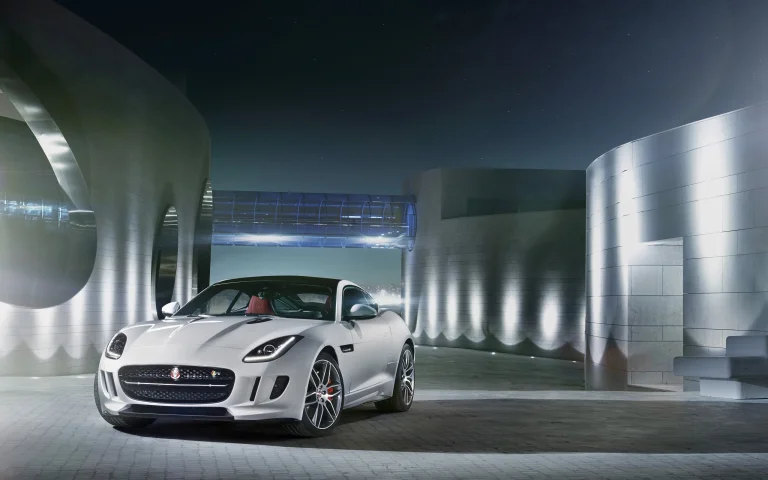 A white Jaguar F-Type against a backdrop of futuristic buildings at night