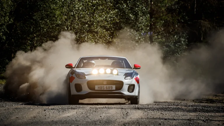 A Jaguar F-Type Rally on a forest gravel road, surrounded by a cloud of dust