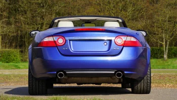 A blue Jaguar XK convertible against the backdrop of a springtime park