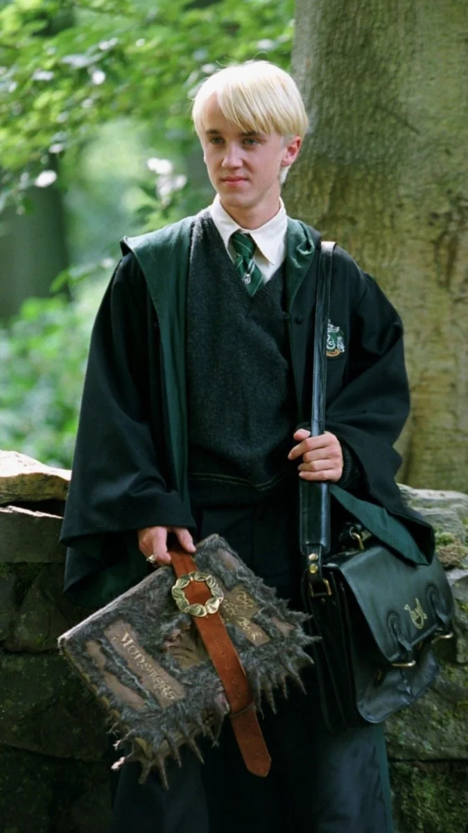 Draco Malfoy in his school robes against the backdrop of a dense forest