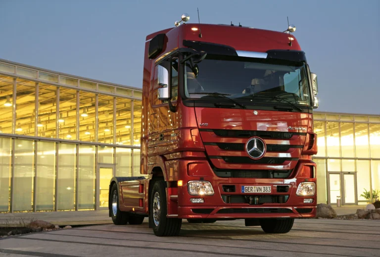 A red Mercedes-Benz Actros tractor-trailer against the backdrop of a modern office building