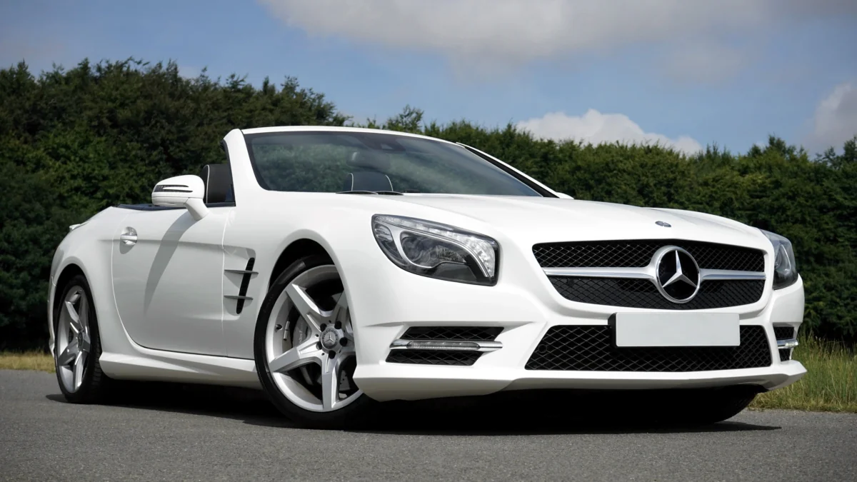 A snow-white Mercedes-Benz SL-Class convertible against a backdrop of summer greenery