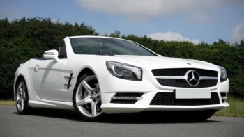 A snow-white Mercedes-Benz SL-Class convertible against a backdrop of summer greenery