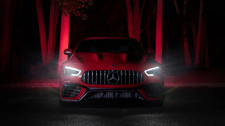 A red Mercedes-AMG GT illuminated by the night lights among the trees