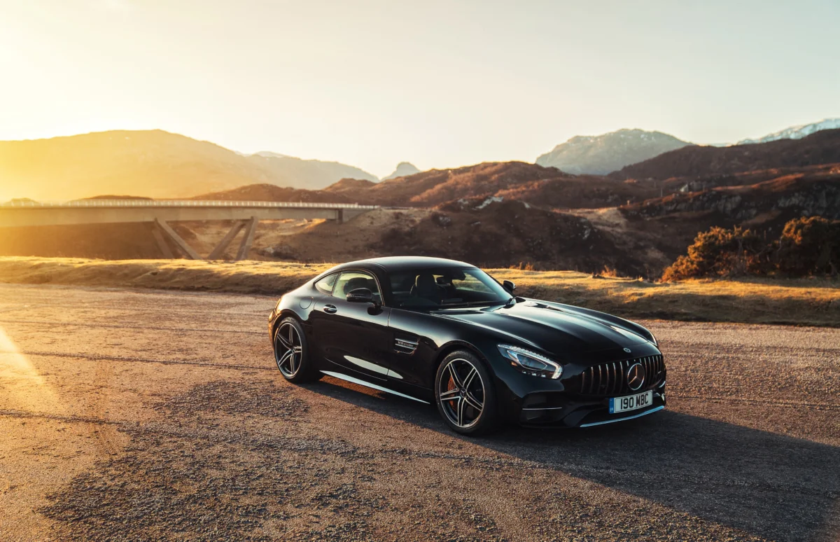 A black Mercedes-Benz AMG GT against a mountain backdrop, bathed in the glow of the sunset