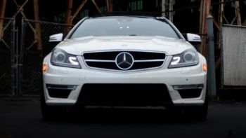 A white Mercedes-Benz C63 AMG against the backdrop of an industrial fence