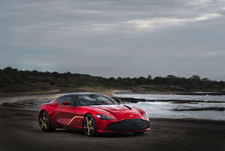 a red aston martin vanquish zagato against the backdrop of the seashore, aston martin vanquish zagato, aston martin, beaches, coasts, cars, automobiles, clouds, discs, wheels, headlights, roads, highways, motorways, avenues, driveways, passageways, sea, sports cars, auto, vehicles