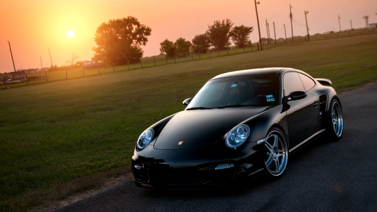 A black Porsche 911 against the backdrop of a field at sunset