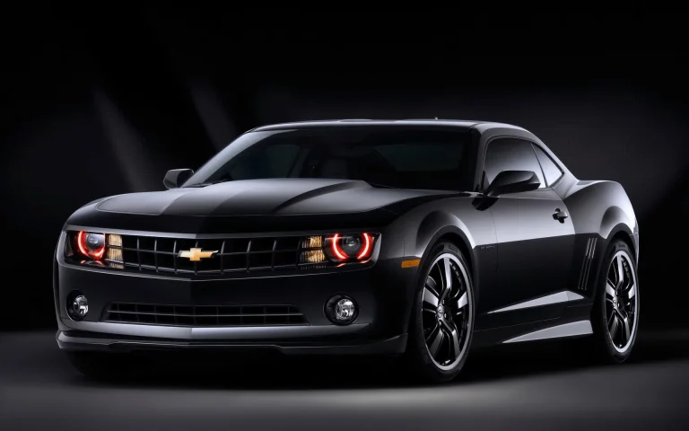 A black Chevrolet Camaro with its headlights on under studio lighting