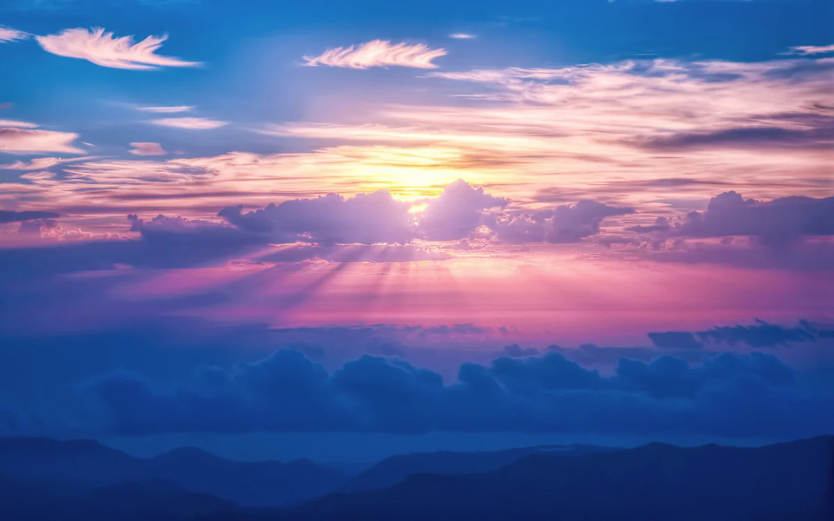 The pink rays of the setting sun over the mountainous horizon