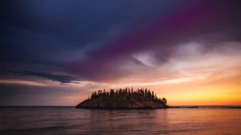 A solitary, wooded island bathed in the rays of the setting sun