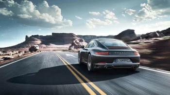 Сірий Porsche 911 Carrera мчить по безлюдній дорозі серед скелястих гір