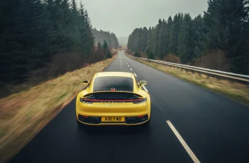 A yellow Porsche 911 Carrera 4S on an empty forest road on a cloudy day