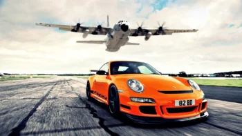 Помаранчевий Porsche 911 GT3 RS на злітно-посадковій смузі під літаком, що пролітає