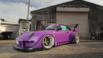 A purple Porsche 911 RWB Rotana next to an industrial hangar