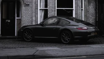 Темний Porsche 911 Carrera S припаркований біля цегляного будинку