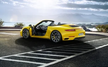 A yellow Porsche 911 Carrera S convertible against the backdrop of the seashore