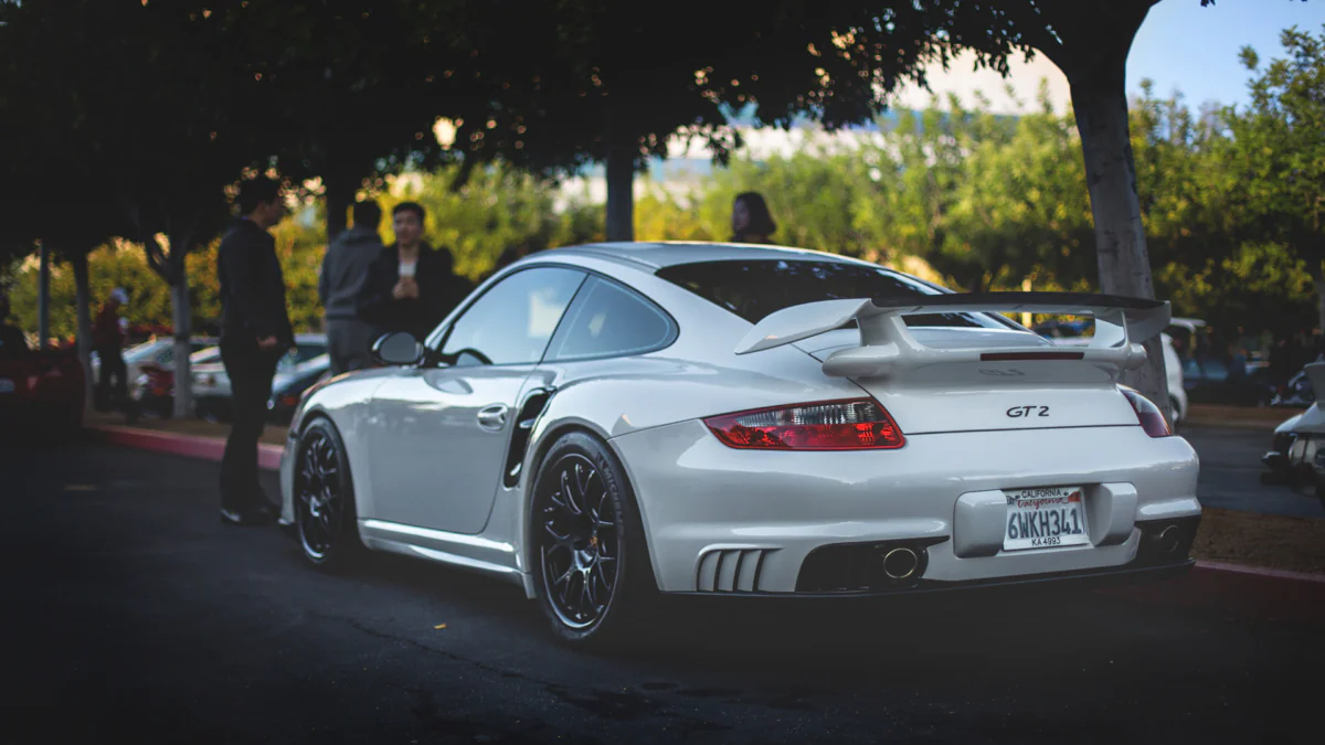 A white Porsche 911 GT2 in a parking lot, shaded by trees