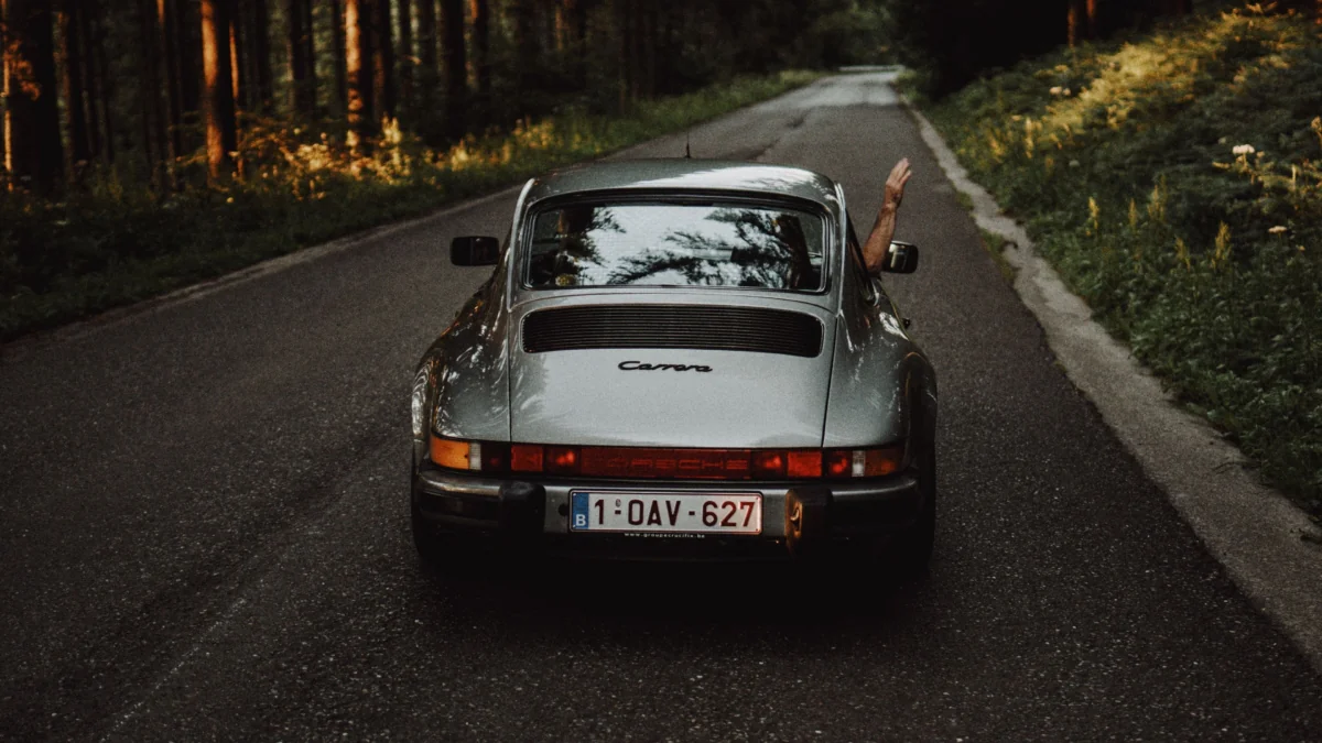 Сріблястий Porsche 911 Carrera їде лісовою дорогою