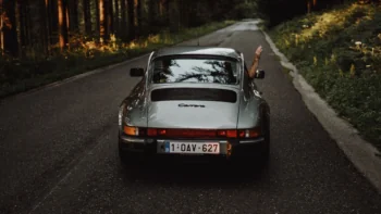 Серебристый Porsche 911 Carrera едет по лесной дороге