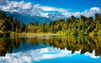 the snow-capped peaks of the southern alps rising above the mirror-like surface of a lake in new zealand, lake matheson and the southern alps, new zealand, clouds, forest, forests, glaciers, lakes, bodies of water, landscapes, mountains, peaks, hills, reflections, trees, nature, world