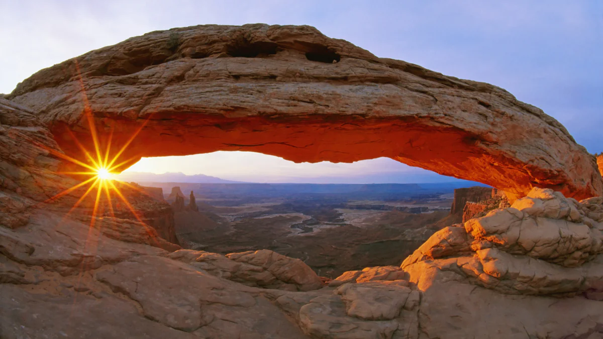 The rays of the rising sun shining through the stone arch of Mesa Arch in the U.S.