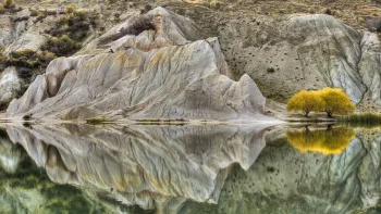 The reflection of rocky hills and yellow trees on the smooth surface of the lake