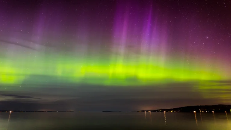 Bright flashes of the northern lights over the calm surface of the water