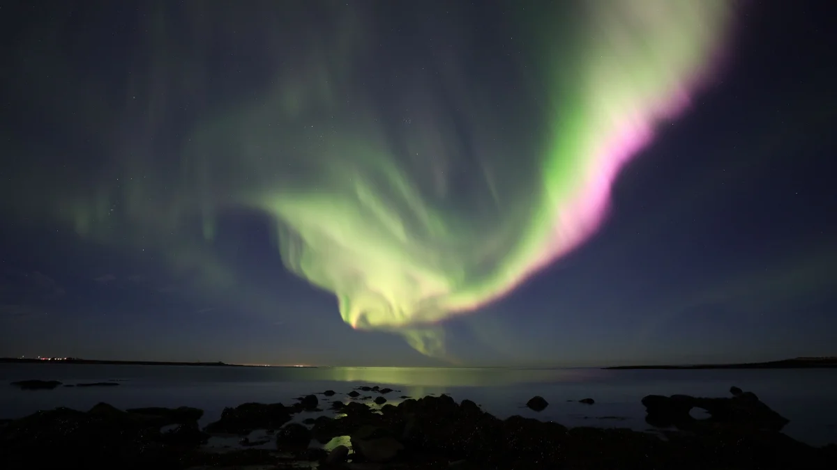 Green flashes of the northern lights over the calm ocean