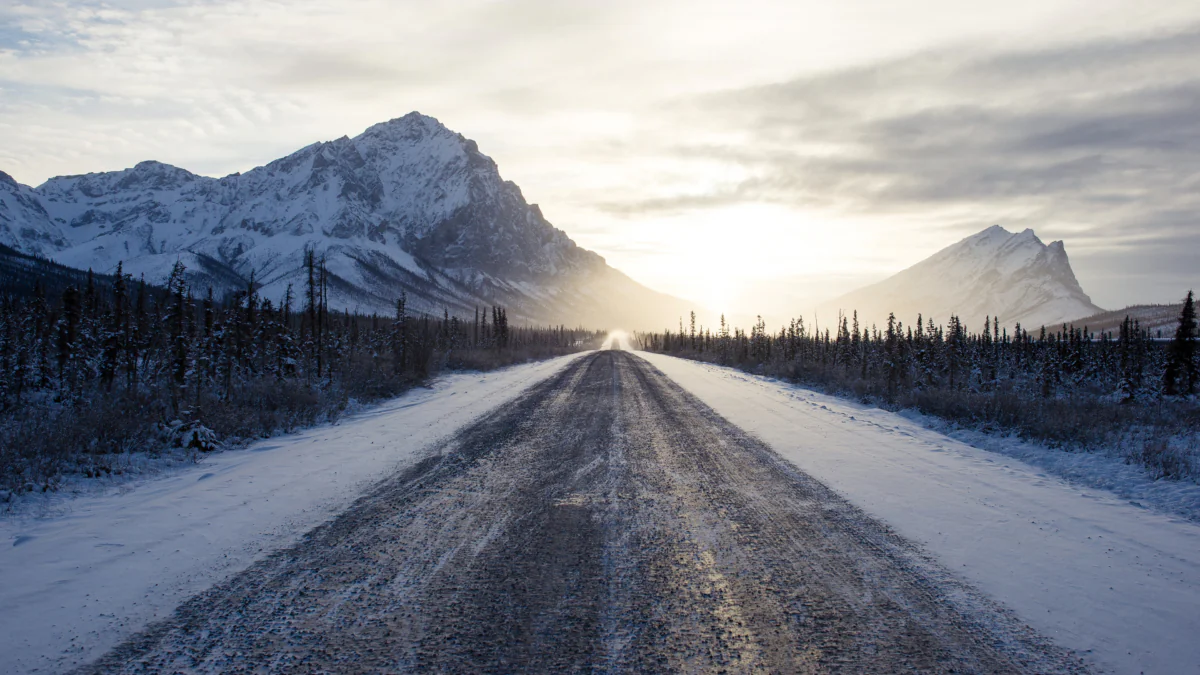 A snow-covered road in Alaska bathed in the rays of the low winter sun