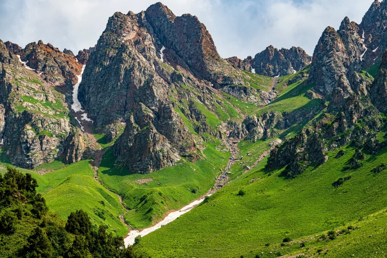 The green slopes of the Tien Shan Mountains with patches of spring snow